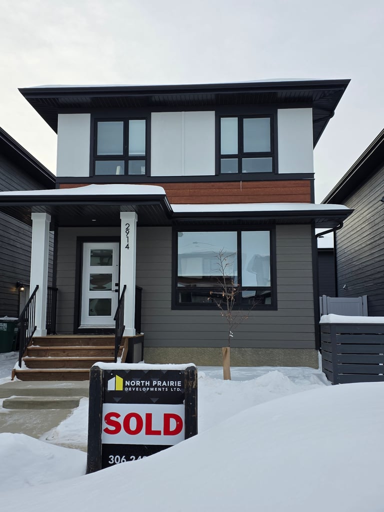 Modern two-story house with gray siding and black trim in winter, featuring a sold real estate sign in the snow-covered front yard