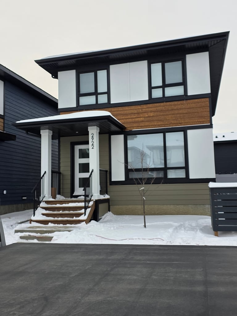Modern two-story house with black and white exterior, wood accent, large windows, and front entrance stairs in winter