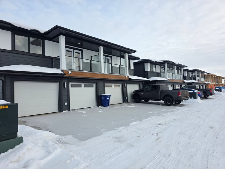 Row of modern townhouses with dark exteriors, white garage doors, and driveways in a snowy winter setting
