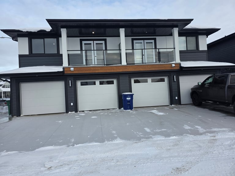 Modern two-story house with black and white exterior, three garage doors, and wooden accent band in snowy winter setting