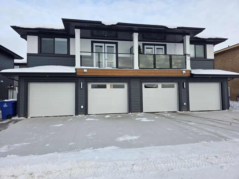 Modern two-story home with black and white exterior, three garage doors, and snowy driveway in winter
